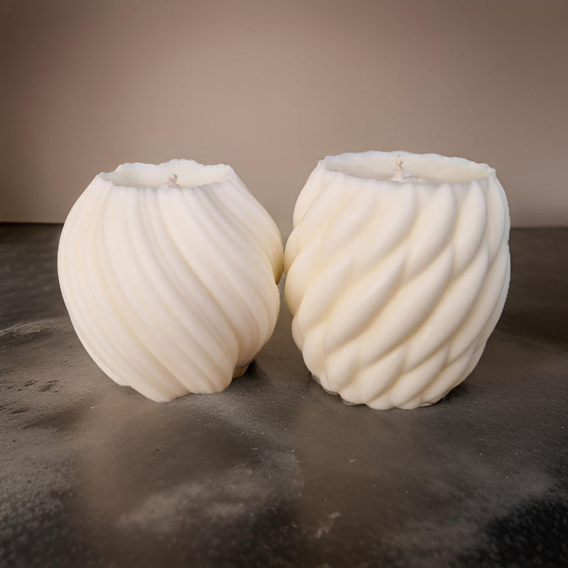 Two white unscented natural wax pillar candles, one lit, providing a soft glow, on a dark background.