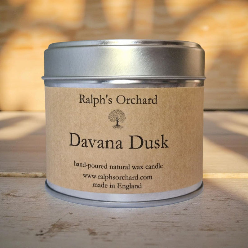 Candle in a tin labeled 'Davana Dusk' by Ralph's Orchard on a wooden surface.