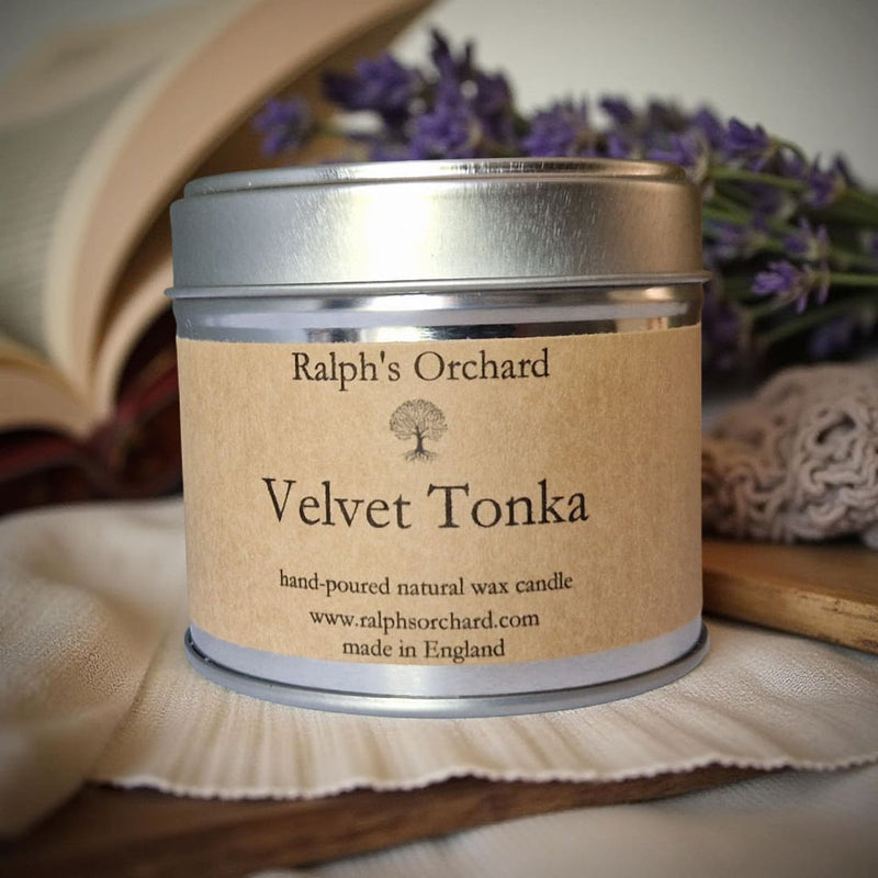 Candle tin labeled 'Velvet Tonka' by Ralph's Orchard with lavender and a book in the background.