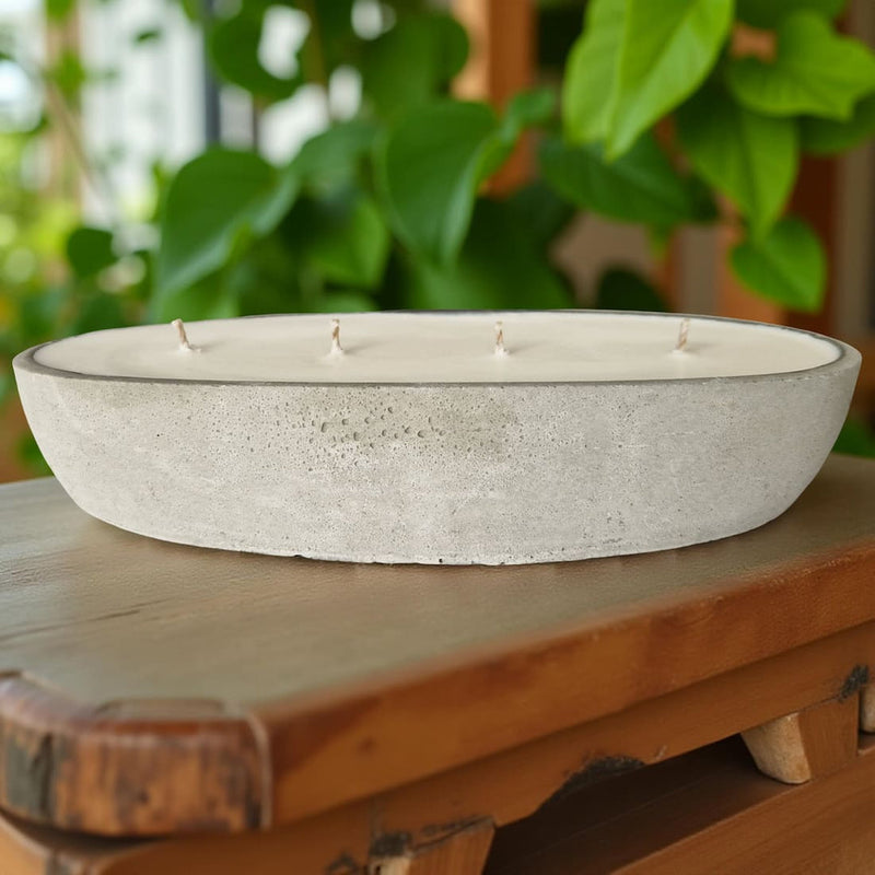 Concrete bowl with candles on a wooden surface with greenery in the background