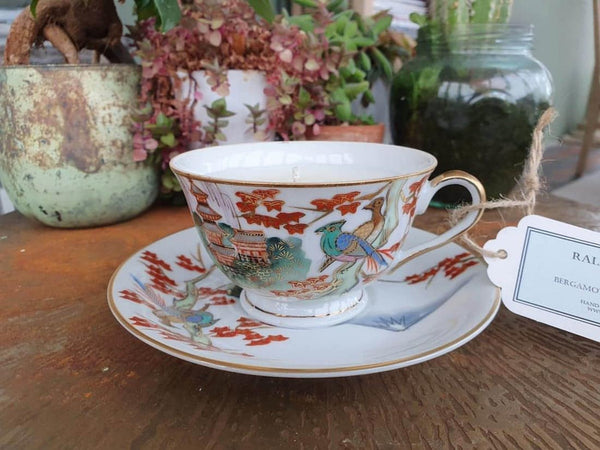 Teacup with decorative design on a saucer, placed on a wooden surface with plants in the background.