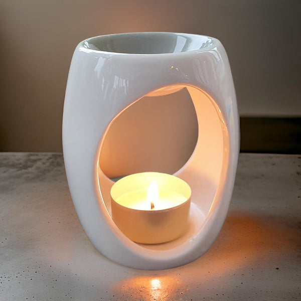 White ceramic oil burner with a lit candle inside on a neutral background