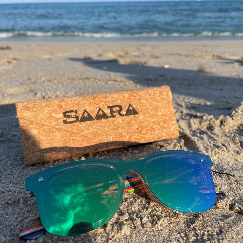emerald sky SAARA shades with rainbow arms sitting in front of the ocean  